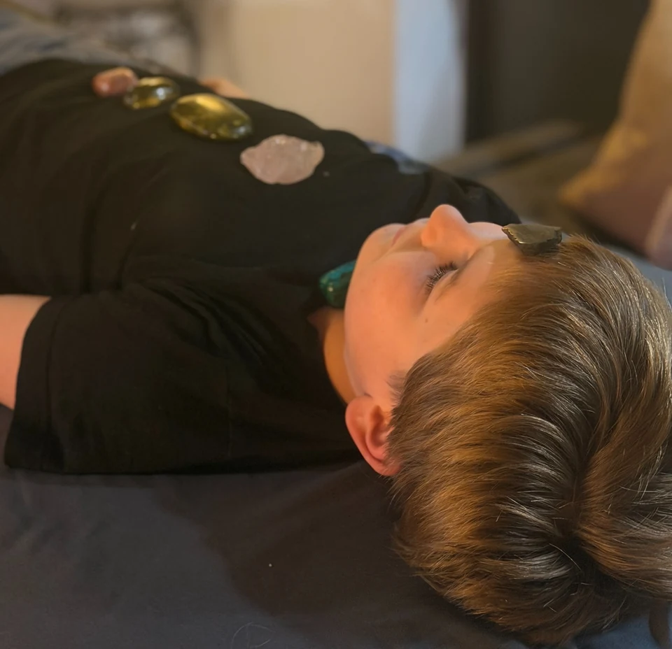 A child resting with eyes closed during a session with crystals on their forehead and over their clothing.