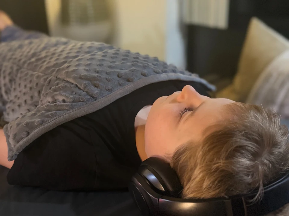 A child resting under a blanket with headphones and eyes closed.